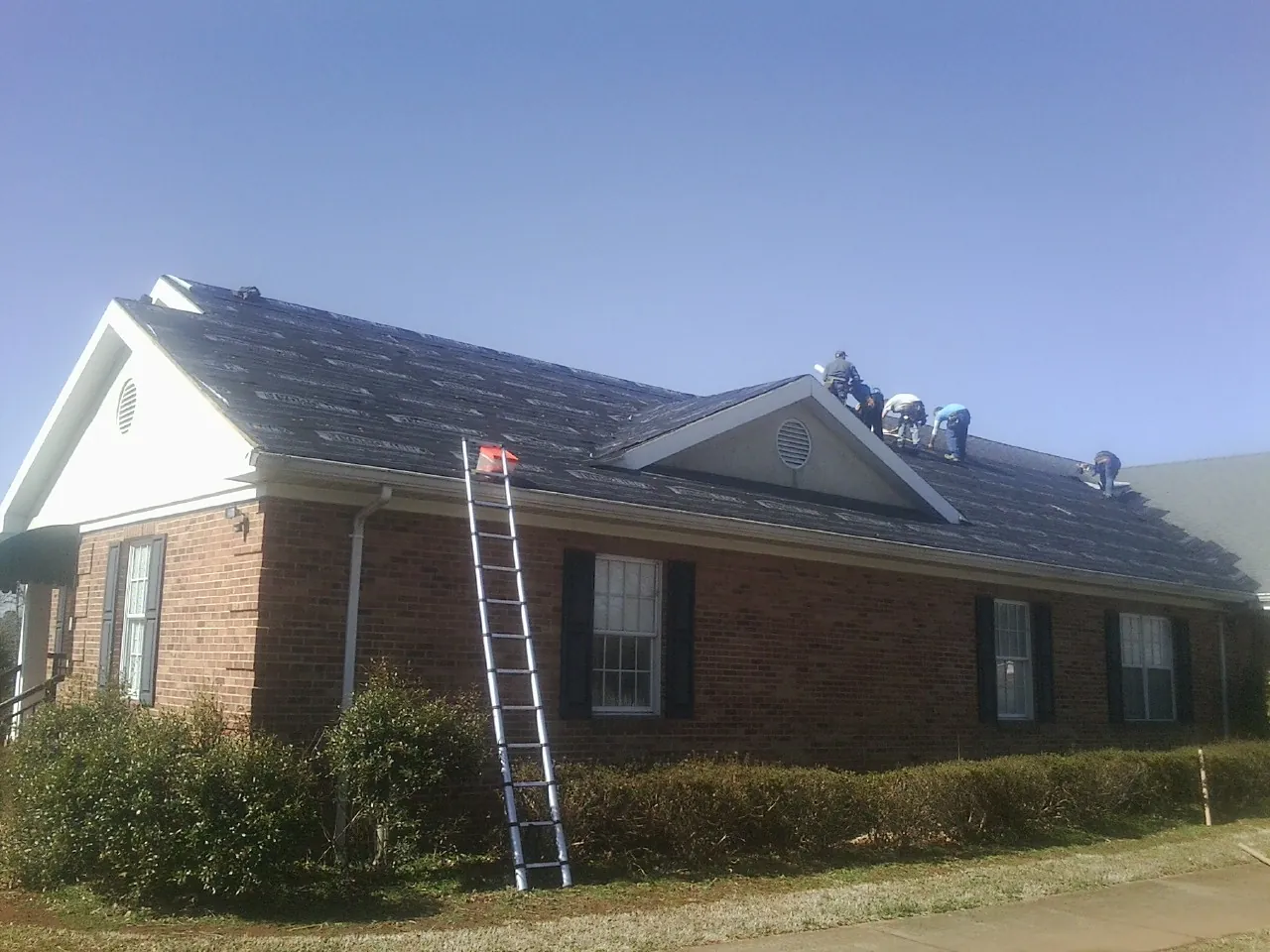 Crew tearing shingles off a brick ranch roof with a ladder set — Metal Roof Repair work by our crew in Fayette City