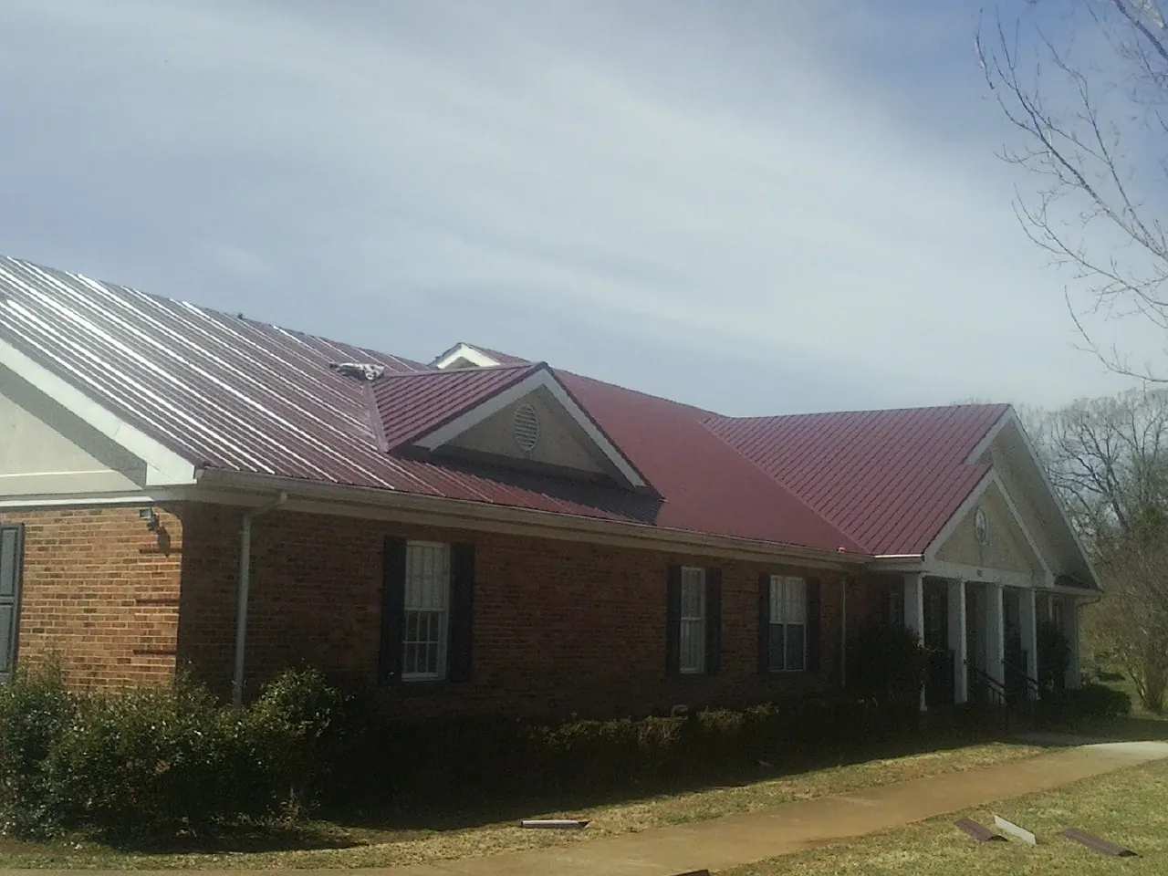 Red metal roof with gabled entries on a long brick building, from a Hail Damage Roof Repair job in Fayette City