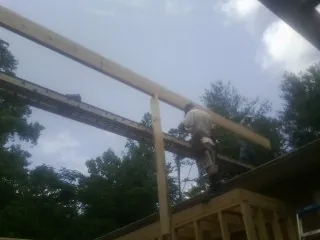 Carpenter setting a ridge beam over a new addition frame in Fayette City