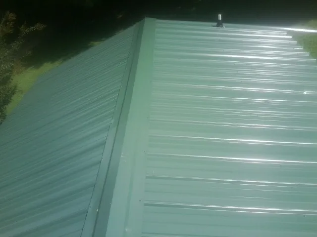 New green metal panels meeting at the ridge of a roof — Flat Roof Repair work by our crew in Fayette City