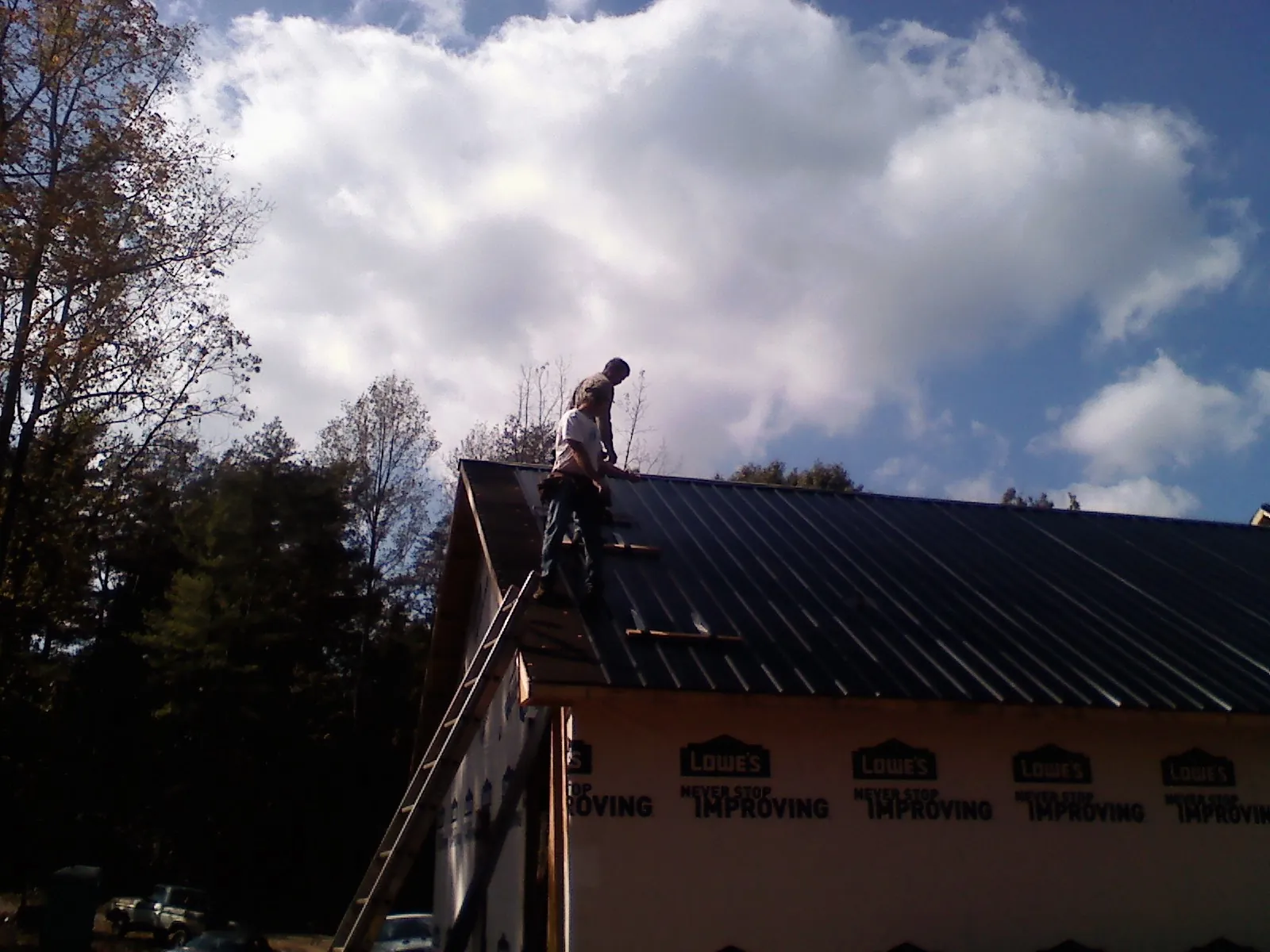 Roofer fastening dark metal panels high against a cloudy sky, from a Roof Inspection job in Fayette City
