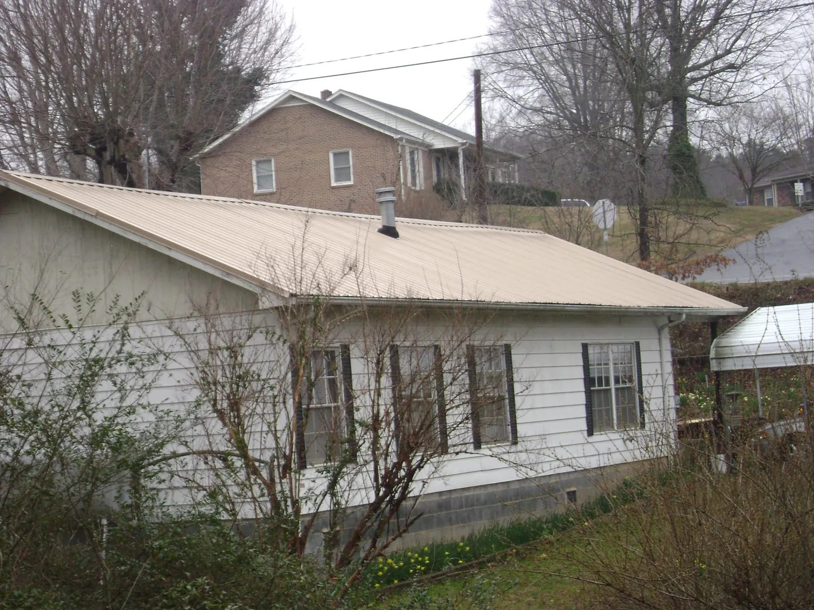 Tan metal roof on a white sided house set into a hillside — Commercial Roofing by Roofing Brothers in Fayette City