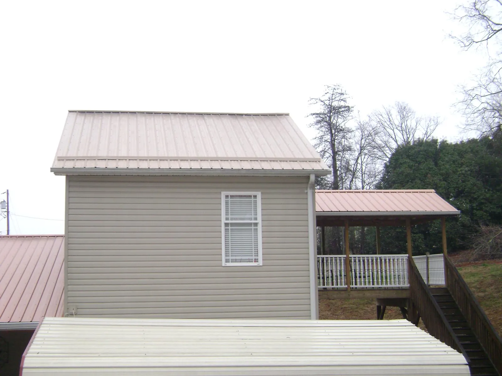 Tan metal roofs on a two story addition and attached porch, from a Roof Replacement job in Fayette City